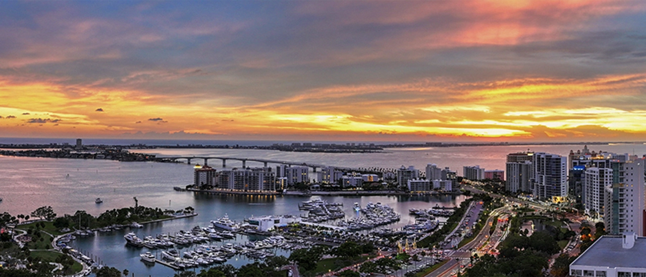 Sunset over Sarasota Bay with downtown skyline, bridge, and marina filled with yachts.