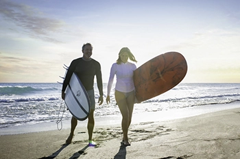 Couple walking with surfboards along a Florida beach at sunrise.