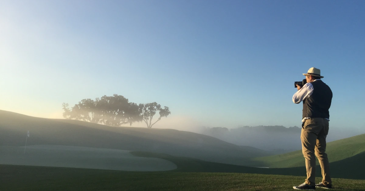 Photographer capturing sunrise on misty golf course