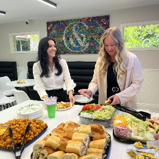 Two women serving food from buffet table with sandwiches and salad