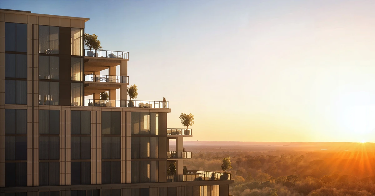 Modern high-rise condo tower with balconies at sunset above a wooded horizon.