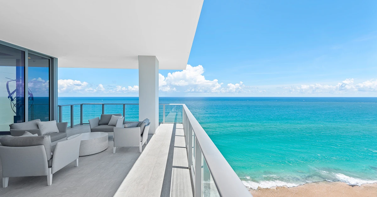 Oceanfront condo balcony with seating overlooking a sandy beach and turquoise water
