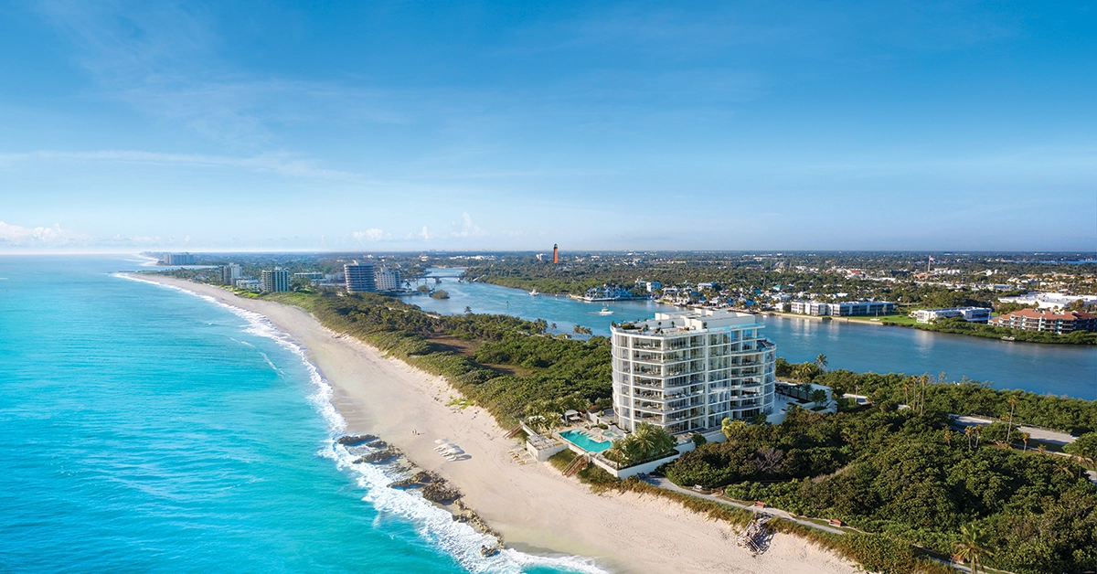 Aerial view of a curved beachfront tower beside turquoise ocean water and an inland waterway.