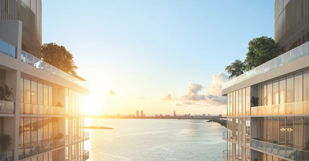 Luxury waterfront residential towers with glass balconies frame a golden sunset over Biscayne Bay with Miamis skyline in the distance