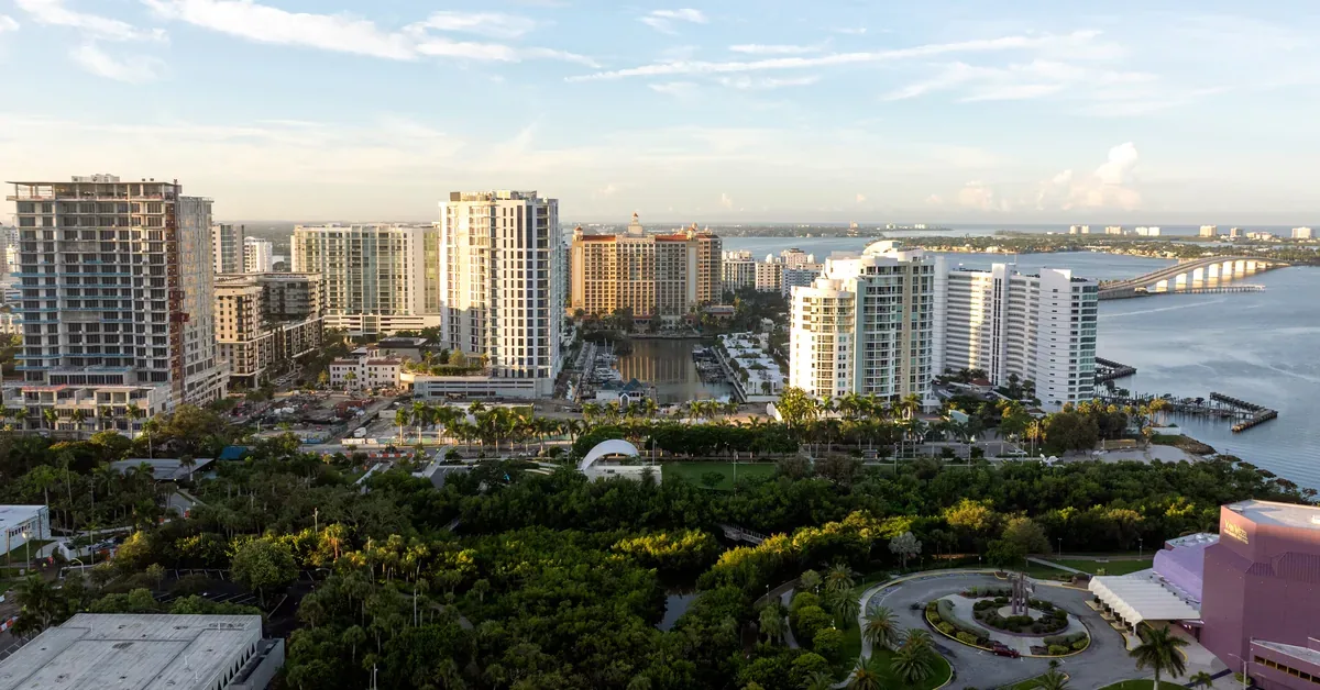 Aerial view of Sarasota's downtown skyline featuring luxury high-rise condos along the sparkling Sarasota Bay waterfront, framed by lush tropical greenery.